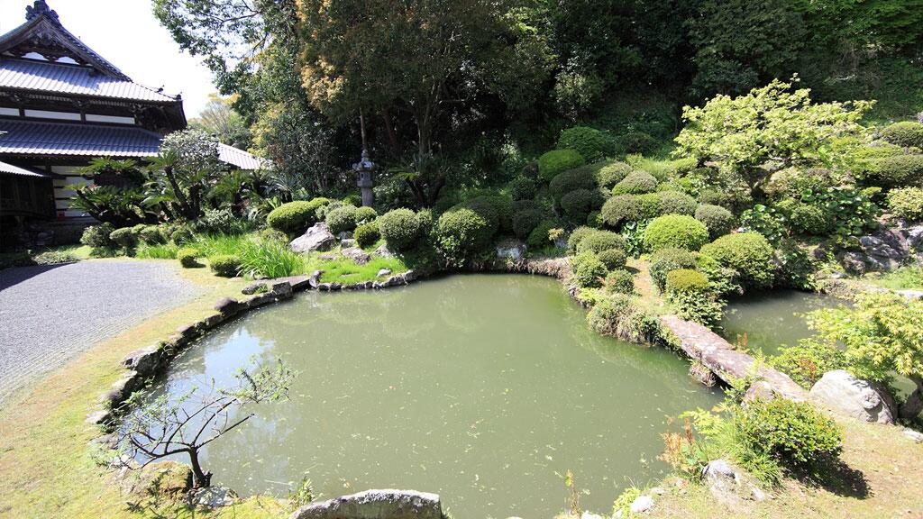 Vijver omringd door groene struiken en bomen in een Japanse tuin.