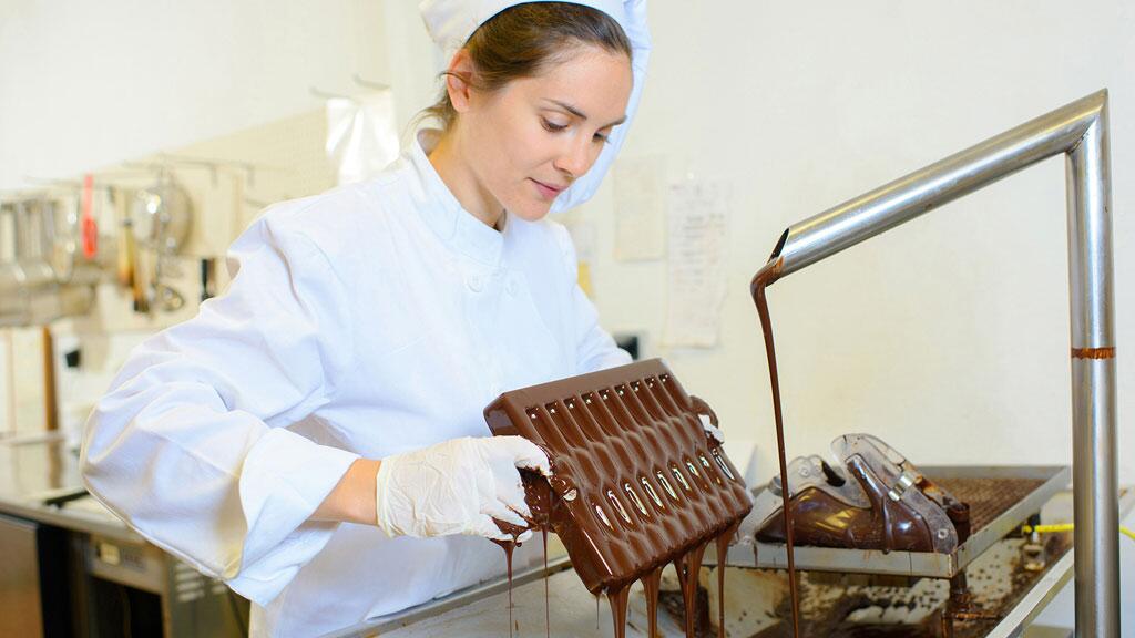 Vrouw in witte jas giet vloeibare chocolade in een mal.