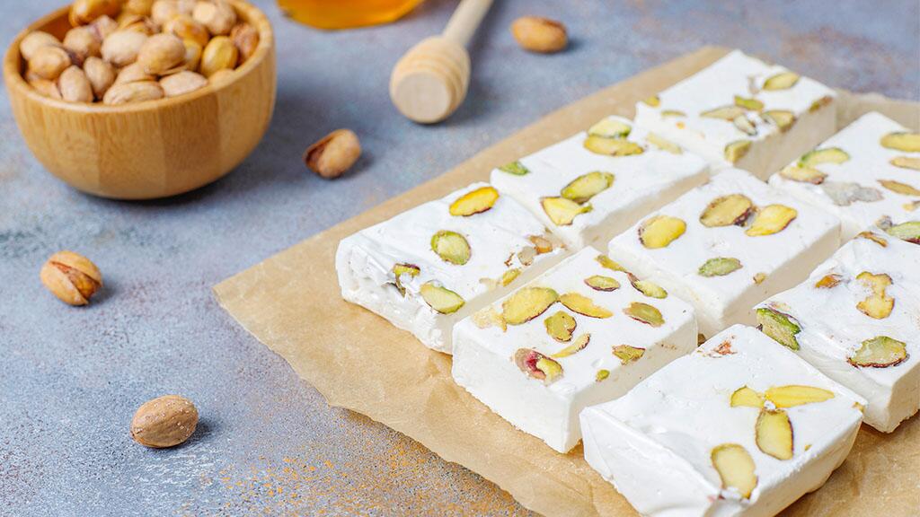 Nougat met pistachenoten op bakpapier, kom met noten op tafel.
