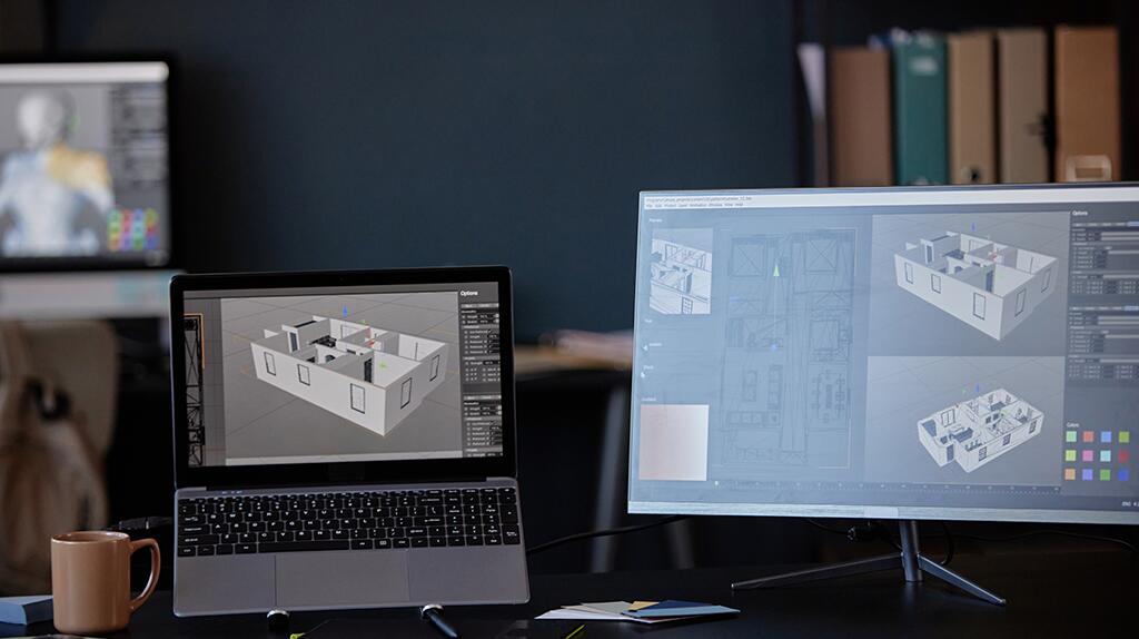 Twee beeldschermen tonen 3D-modellen van architectuurontwerpen in een kantoorruimte.