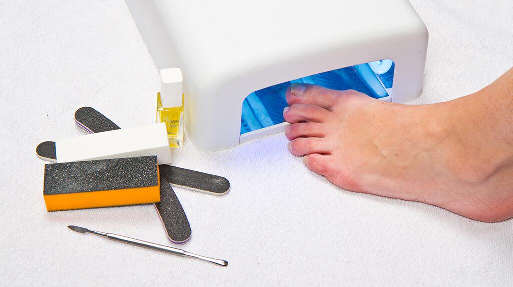 Voet onder UV-lamp met manicuretools ernaast.
