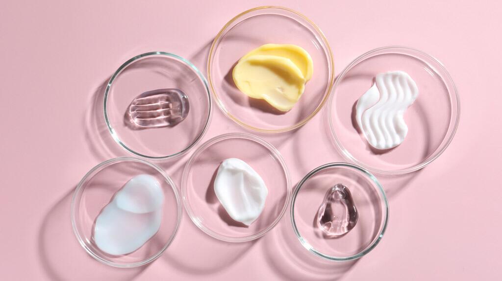 Glazen schaaltjes met verschillende cosmetische crèmes op roze achtergrond.