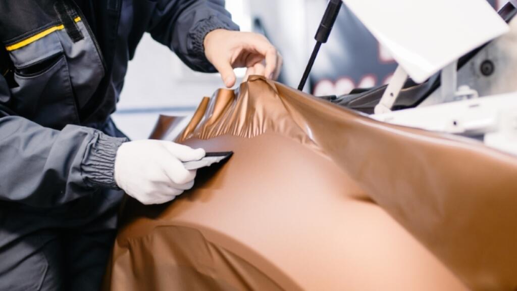 Handen in witte handschoenen wikkelen een bruine folie om een auto.