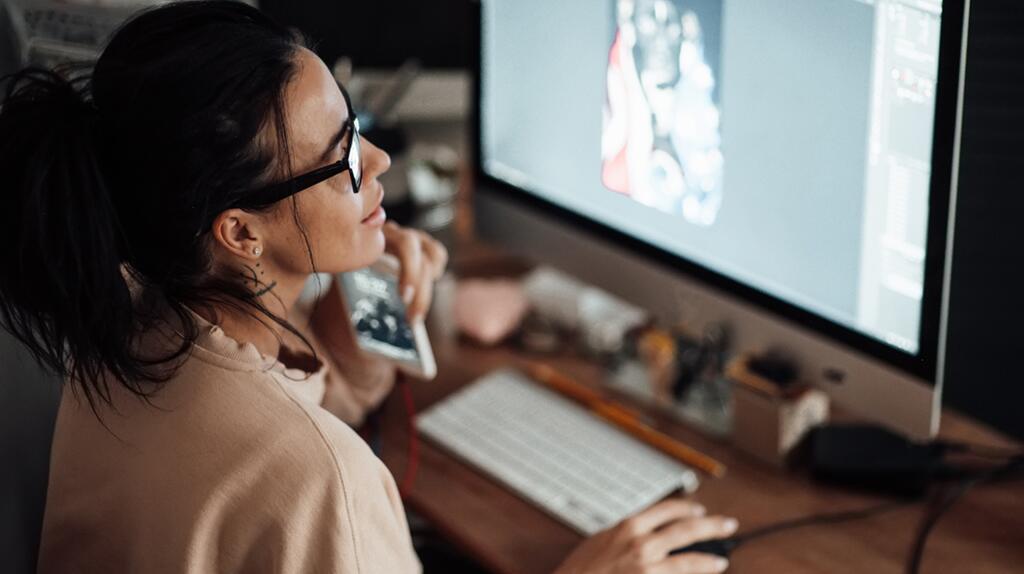 Vrouw met bril werkt op computer, potlood in de mond.