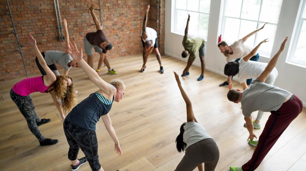 Groep mensen doet zijwaartse stretch in een lichte studio.