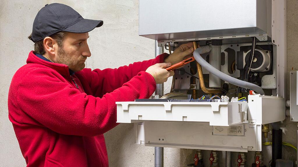 Monteur in rood werkend aan verwarmingsketel.