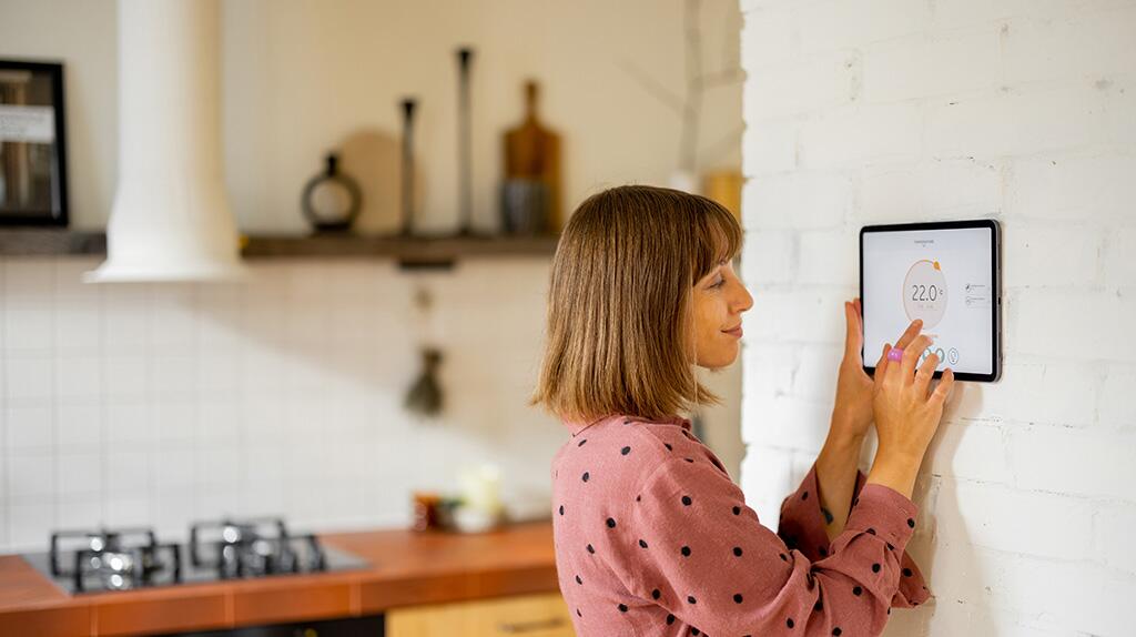 Vrouw bedient tablet aan muur in lichte keuken.