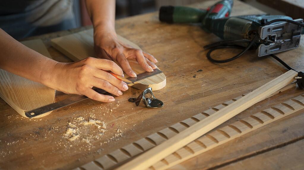 Handen bewerken hout op werkbank met gereedschap en schuurpapier.