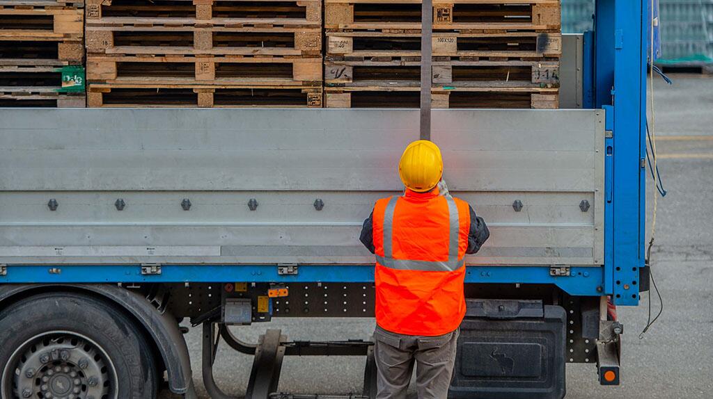 Werkman met veiligheidshelm laadt pallets op vrachtwagen.