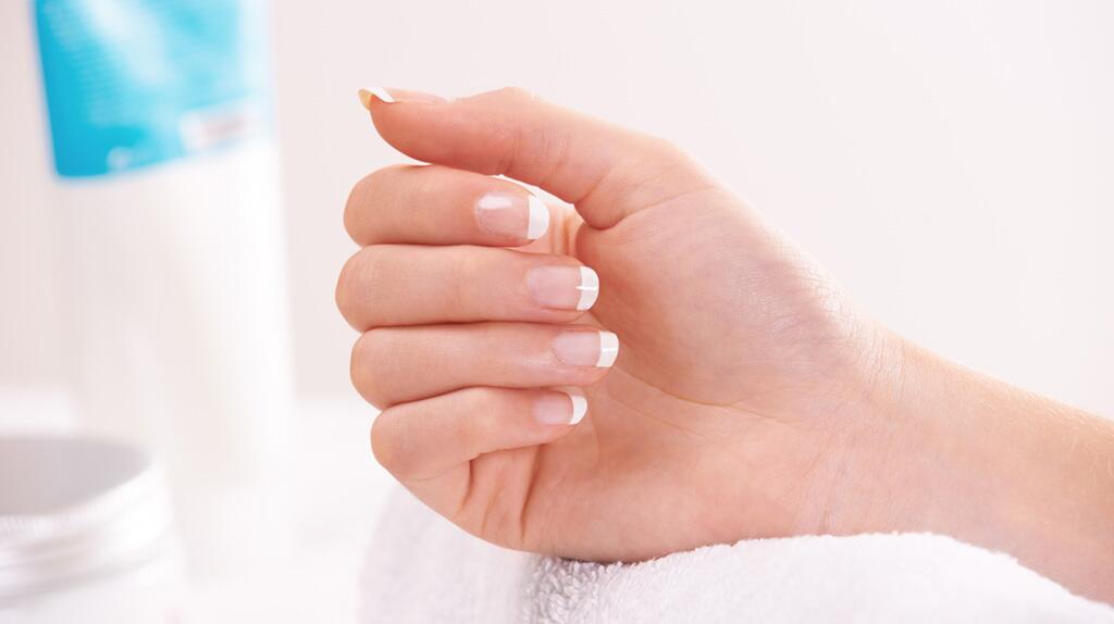 Hand met Franse manicure tegen een wazige achtergrond.