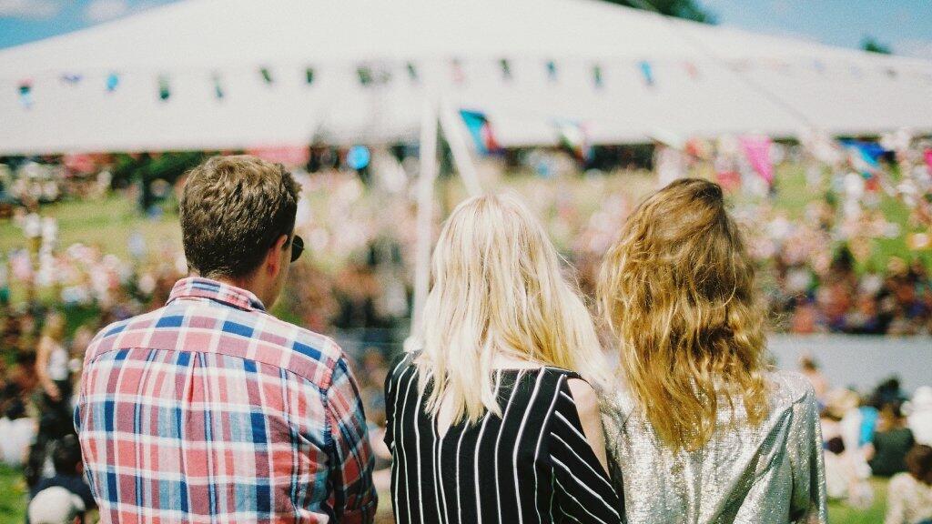 Drie mensen van achteren, kijkend naar een festival met een grote tent.