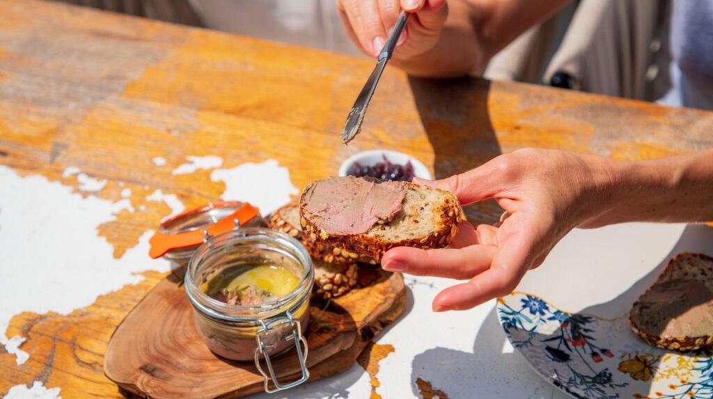 Hand smeert jam op een snee brood bij een houten plank met honingpot.