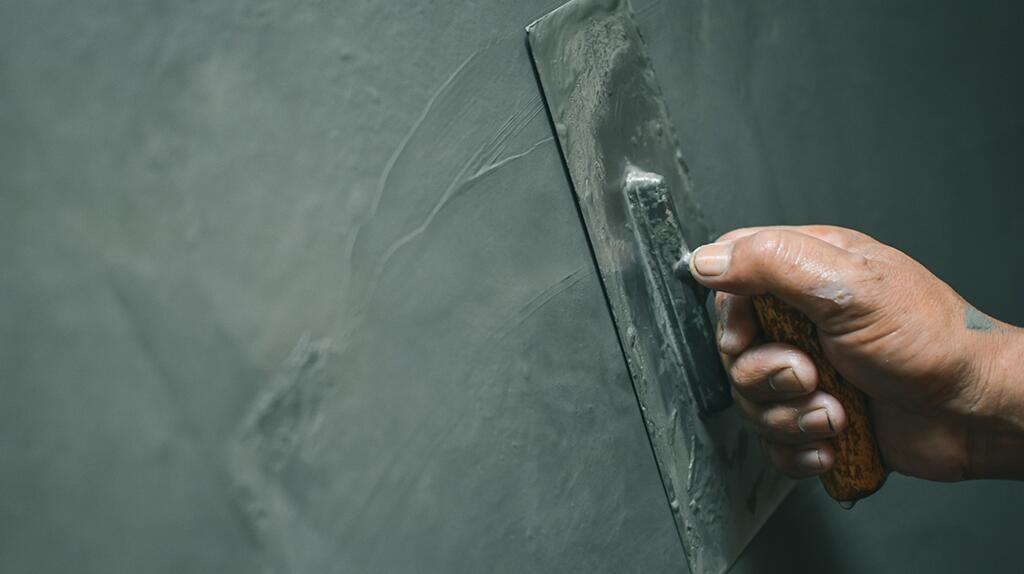 Hand schuurplank op grijze muur.