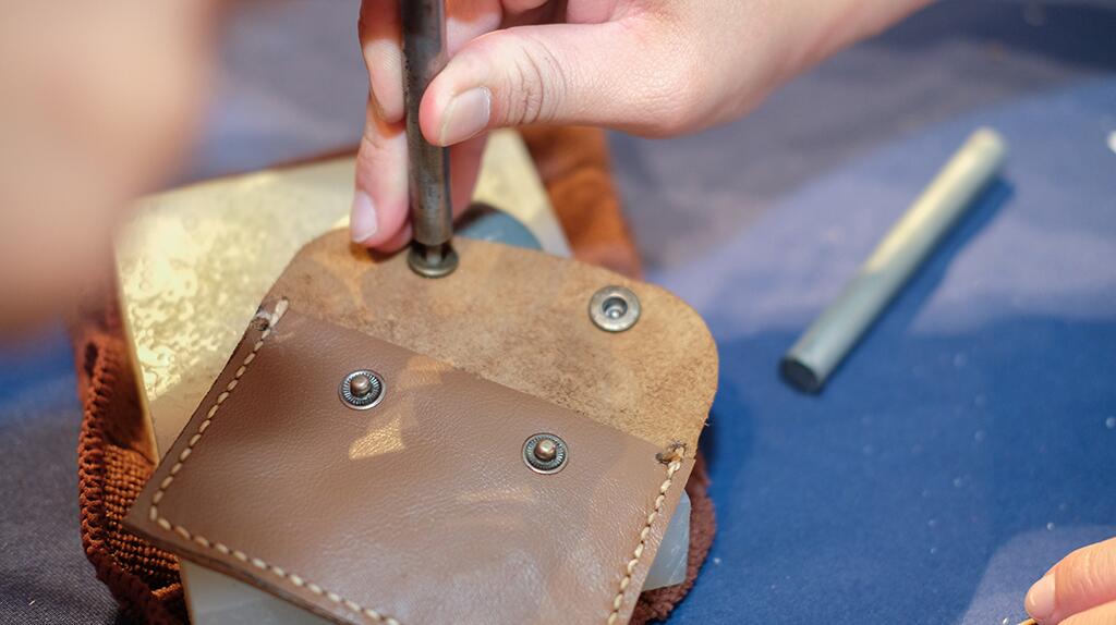 Leren tas wordt met drukknopen bevestigd. Hand houdt gereedschap vast.