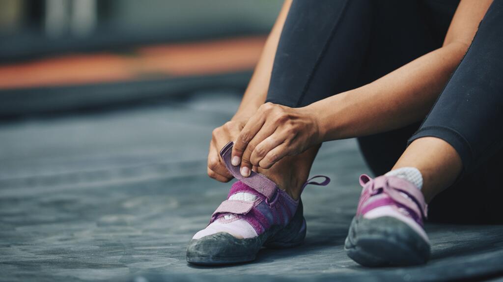 Persoon strikt paarse klimschoenen op donkere vloer.