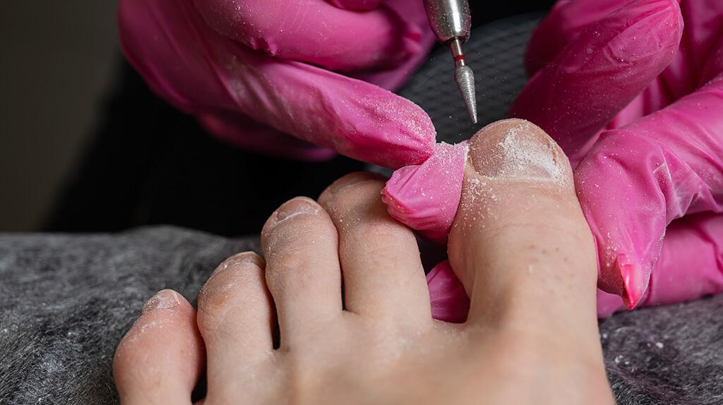 Pedicurebehandeling, roze handschoenen en elektrische vijl.