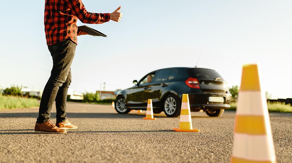 Man met clipboard geeft duim omhoog naar auto tussen verkeerskegels op zonnige dag.