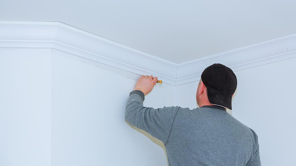 Man schildert witte kroonlijst aan plafond.