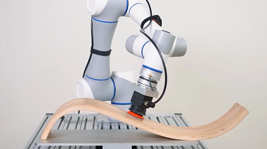 Robotarm bewerkt een gebogen houten stuk op een werkblad.