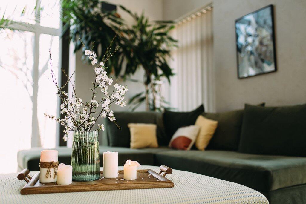 Moderne woonkamer met groene bank, kussens en planten. Koffietafel met kaarsen en bloemen.