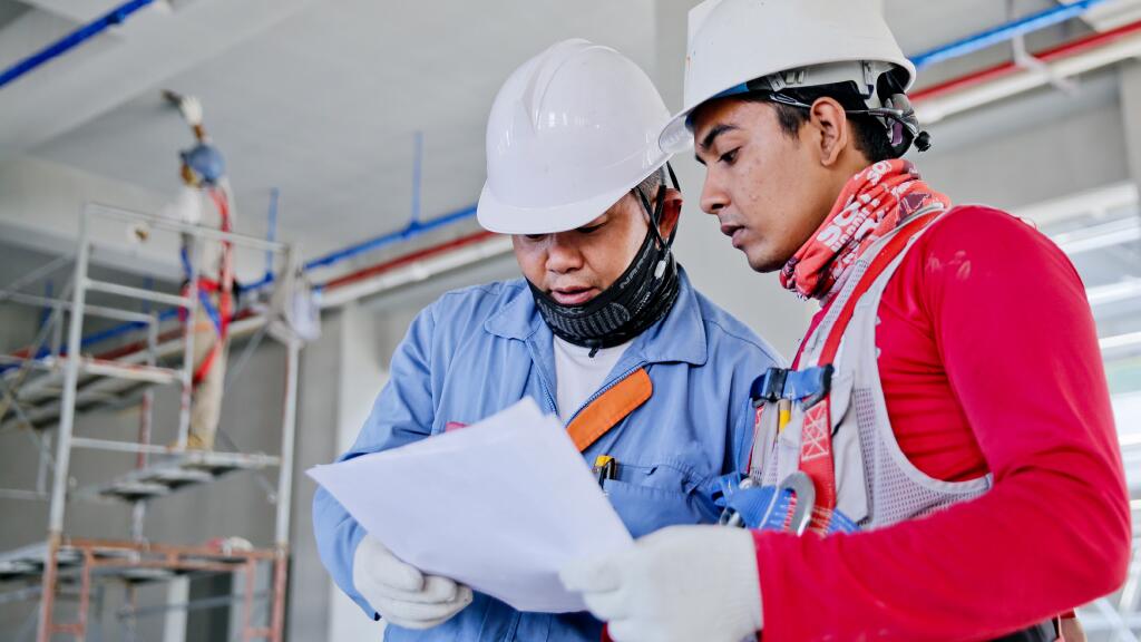 Bouwvakkers in helm bekijken een plan in een bouwplaats.