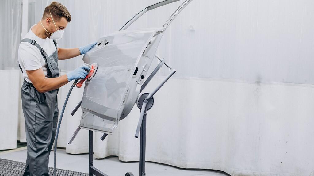 Man in overall schuurt autodeur in werkplaats.