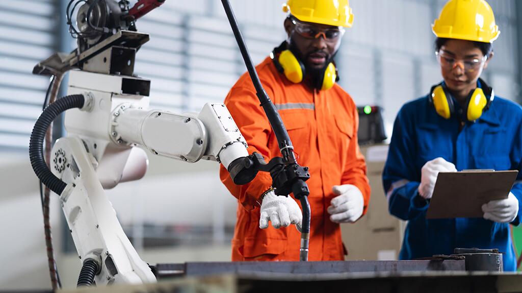 Twee fabriekswerkers in veiligheidskleding inspecteren een robotarm.