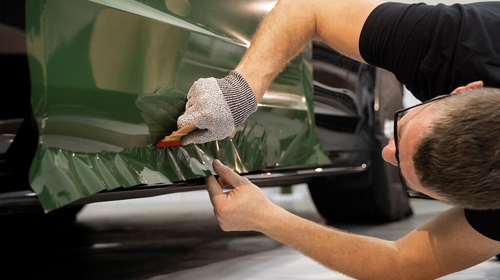 Man brengt groene folie aan op een auto, nauwkeurig werkend met een gereedschap.