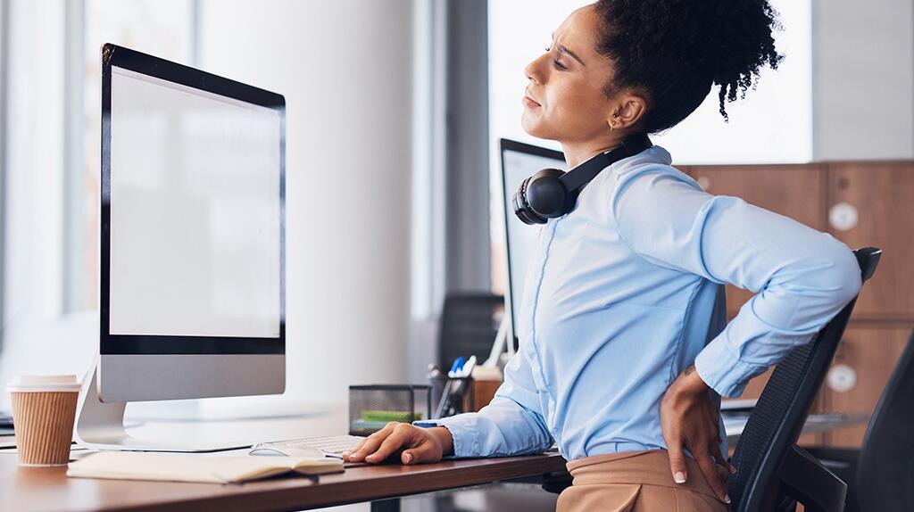 Persoon met rugpijn aan bureau met computer, draagt hoofdtelefoon.