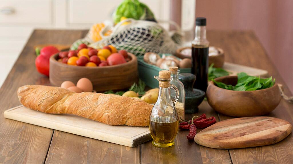 Vers brood met olijfolie, groenten, fruit en kruiden op houten tafel.