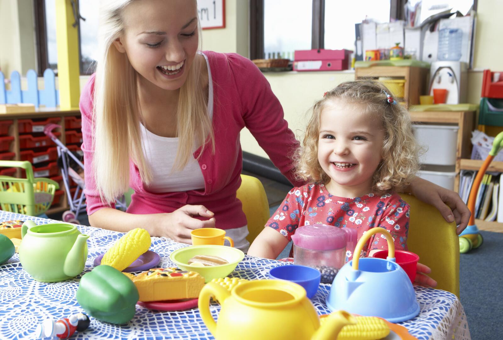 Volwassene en kind spelen met speelgoedservies in kleuterklas.