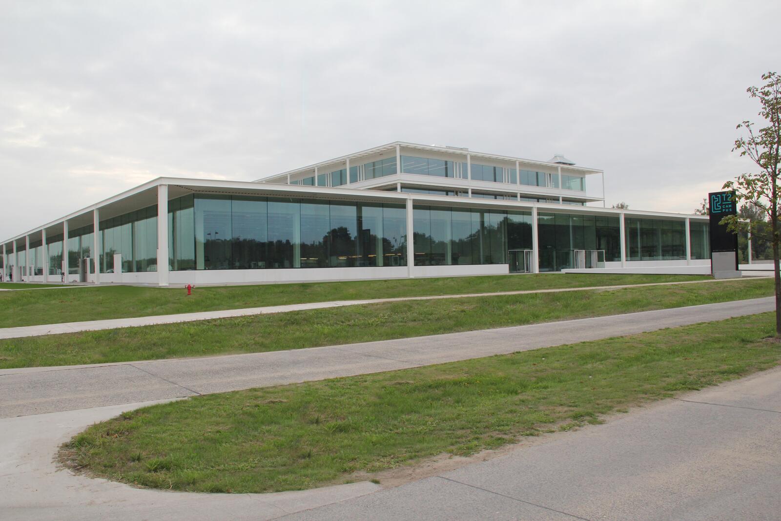 Modern glazen gebouw met groen grasveld ervoor.