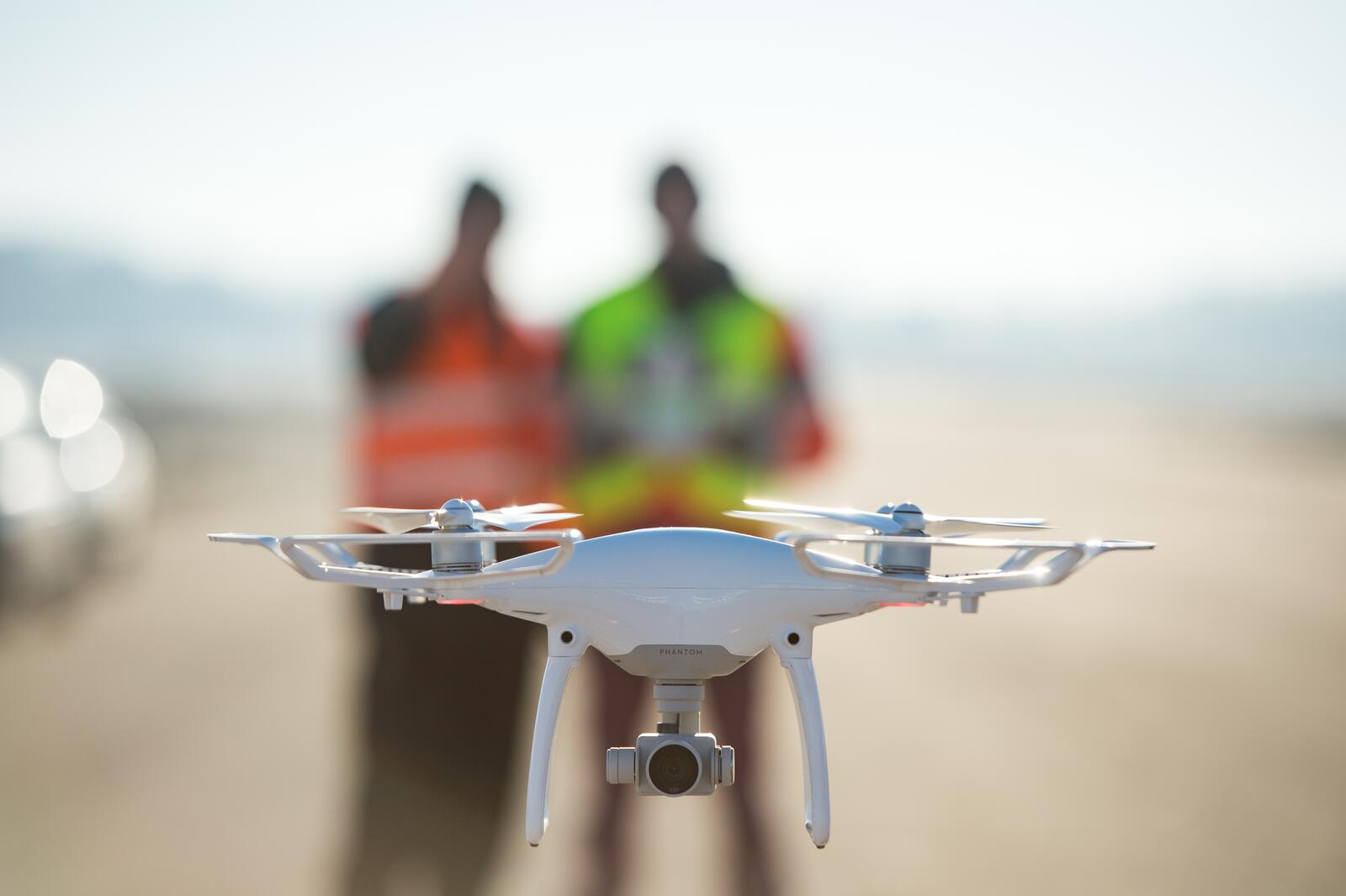 Witte drone op de voorgrond, twee personen in veiligheidskleding op de achtergrond.