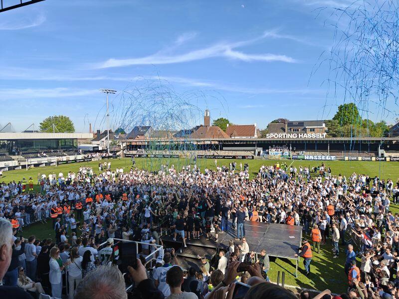 Massa mensen op een festivalterrein met blauwe lucht en confetti in de lucht.