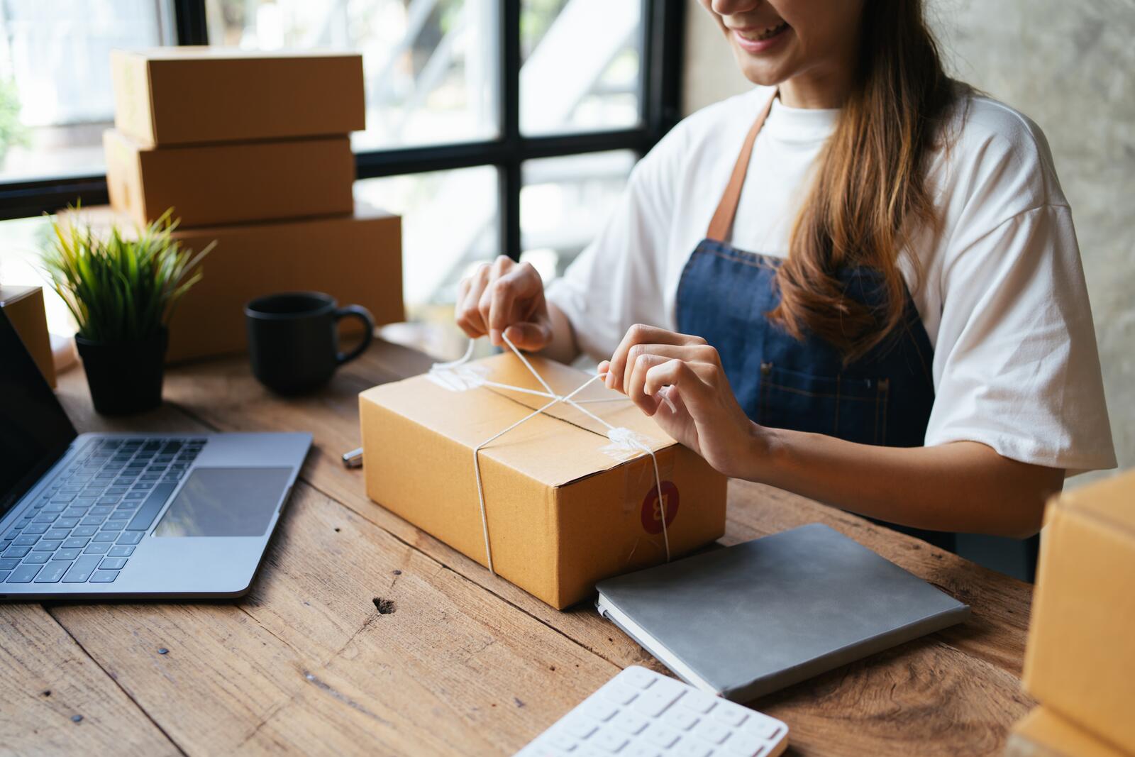 Vrouw verpakt een doos in een kantoor aan een houten tafel met laptop.