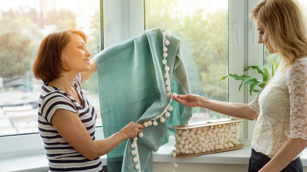 Twee vrouwen bekijken een turkoois gordijn met sierlijke details bij een raam.