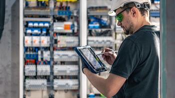 Technicus met tablet inspecteert elektrische schakelkast.