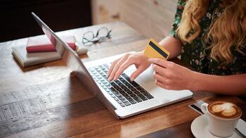 Vrouw winkelt online met laptop en creditcard, koffie op tafel.