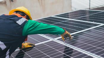 Persoon installeert zonnepanelen met een veiligheidshelm en handschoenen.