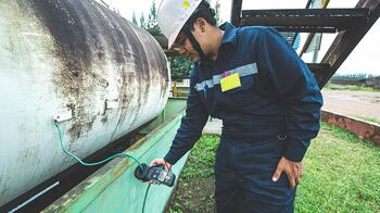 Man in werkpak controleert een grote metalen tank met een apparaat.
