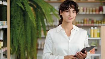 Vrouw met tablet in winkel, omringd door planten en producten.