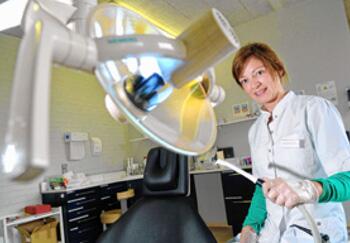 Vrouwelijke tandarts in kliniek met grote lamp.