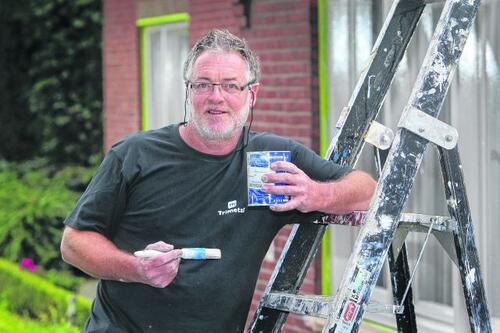 Man met verfkwast en blik bij ladder voor een huis.