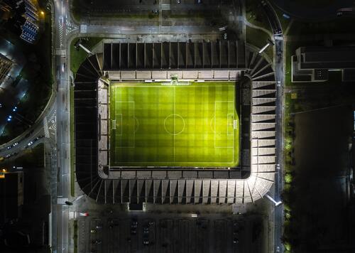 Nachtfoto van een verlicht stadion van bovenaf, groene grasmat centraal.