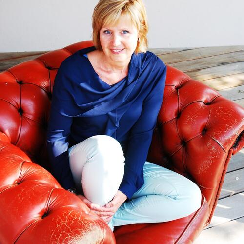 Vrouw in blauwe blouse op rode leren bank, glimlachend.
