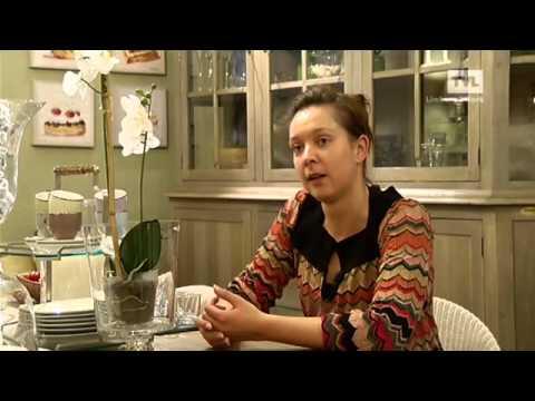 Vrouw zittend aan een tafel met bloemendecor, houten kast op de achtergrond.