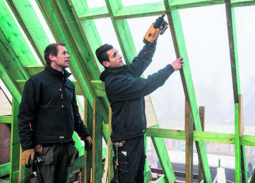 Bouwvakkers werken aan een groen houten dakconstructie.