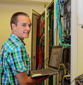 Man werkt op laptop bij serverkast met kabels.