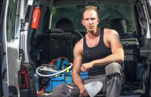 Man in een bestelwagen met gereedschap, draagt een zwarte tanktop.