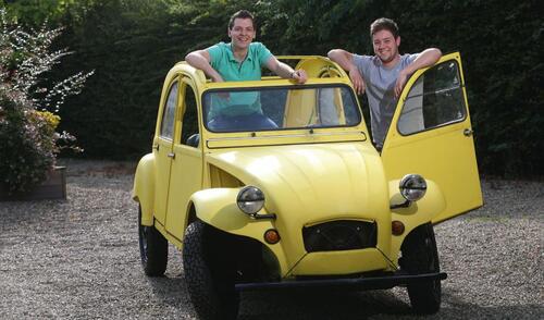Twee mensen in een gele oude auto, portieren open, glimlachend.
